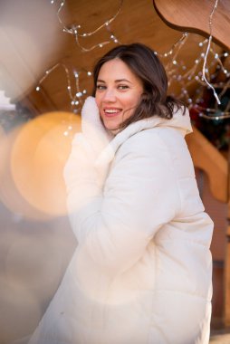 Adil. Beyaz ceketli ve beyaz şapkalı bir kız. Kız gülümsüyor. Elde bir fincan kahve. Ahşap yazlık. Kız seviniyor. duygular.