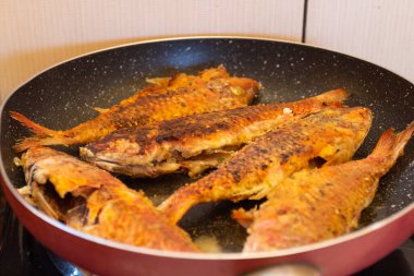 Mutfaktaki gaz sobasında kızartma tavasında kızarmış balık.