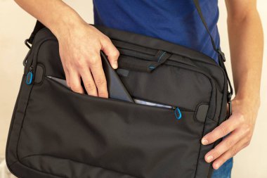 Akıllı telefon ve laptop çantası. Adam bir çantaya akıllı telefon koyuyor, bilgisayar taşıma konsepti, akıllı telefon, dizüstü bilgisayar için koruyucu klasör.