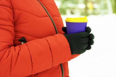 Kollar kahve ve kağıt bardak tutuyor. Karlı arka planda tek kullanımlık bir bardak tutan eller. Kış konseptine uygun kahve. Sıcak ve sıcak içecekler kış konseptinde.