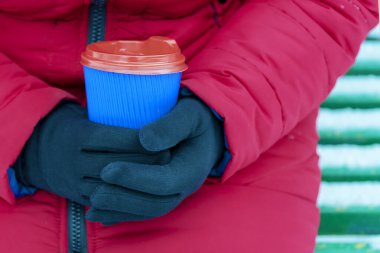 Kollar kahve ve kağıt bardak tutuyor. Karlı arka planda tek kullanımlık bir bardak tutan eller. Kış konseptine uygun kahve. Sıcak ve sıcak içecekler kış konseptinde.