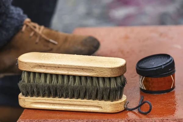 Shoe cream, brush close-up. Cleaning of boots on the street. Concept wrong care of footwear. Man\'s right foot shoe on traditional style boot scraper with brushes