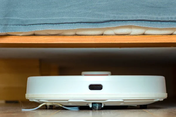 White robot vacuum cleaner.robot vacuum cleaner under the bed.