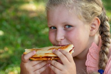Neşeli kız turta yiyor. Elinde bir dilim pizza tutan mutlu çocuk. Çocuklar için yiyecek kavramı, piknik