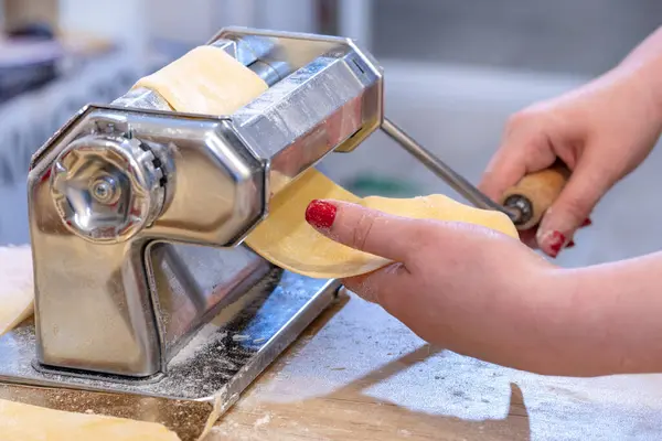 Pasta maker. dough. Woman\'s hand. The concept of making dough and pasta at home. Preparing fresh  rolling dough with a pasta Machine.