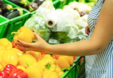 Kız elinde tatlı biber tutuyor. Kadın eli marketten sarı sebze alıyor. Yakın plan. Kadın bir mağazadan sebze seçiyor. Konsept alıcılar, alışveriş konsepti. biber almak