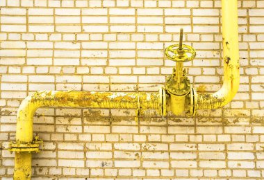 Sarı gaz borusu. Kapı mandalı, borudaki vinç. Tuğladan bir duvarın arka planına karşı Gaz ikmali. valf borusu