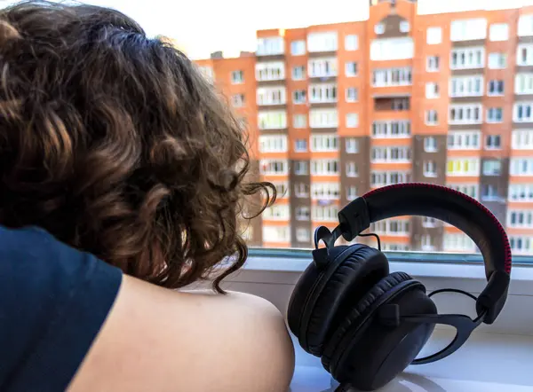 Girl in headphones looking out the window. headphones close up. earphones by the window