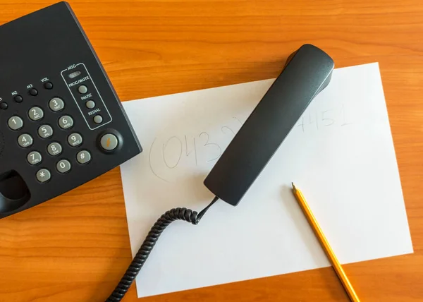 The black desktop push-button telephone on desk in office. Black phone with a tube on the table. top view. Handset and pencil on white sheet. communication concept. close-up