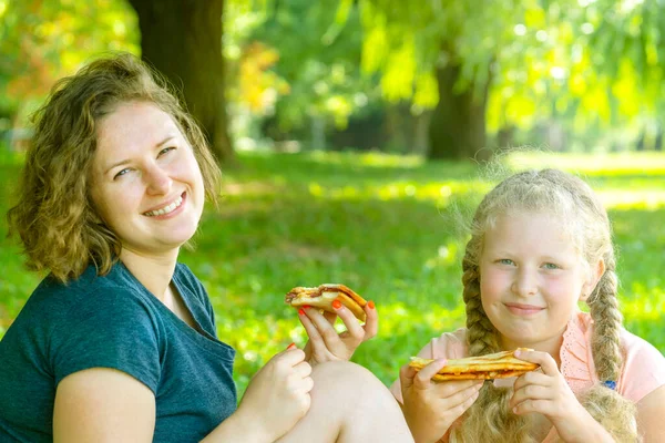 Mother and the daughter eat pie. family picnic. The  woman and the girl together eat  pie. Concept of leisure of family, outdoors, picnic