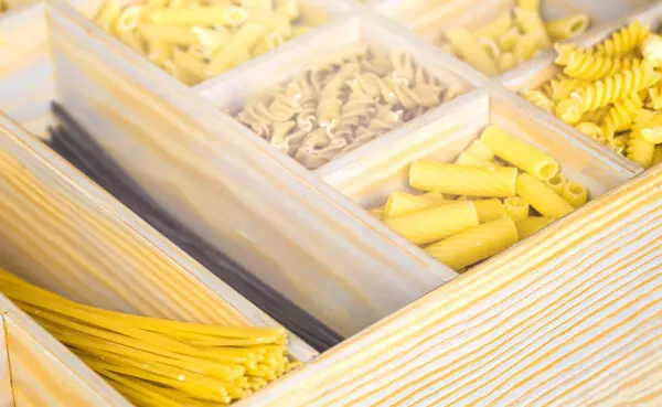 Assorted pastas in wooden box. Italian pasta collection on rustic wooden table. Different types of macaroni, pasta dry.
