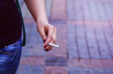 Kadın elinde bir sigara tutuyor. Sigara konsepti, sigara tiryakisi. Yakın çekim. Kadınların ölüm tehdidi. Bağımlılık. Sigara içmeyi bırakmak. Sosyal sorun..