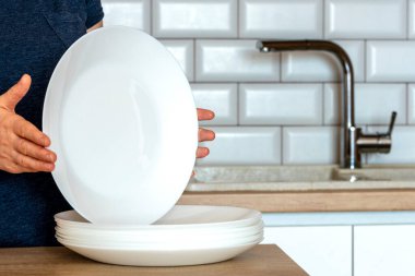 Bir kadın elinde bir tabak tutuyor. Temiz bulaşıkları olan bir ev hanımı. - Mutfak, bulaşıkçı. Tabaklar, bardaklar. Bulaşık yıkama kavramı, temiz tabaklar