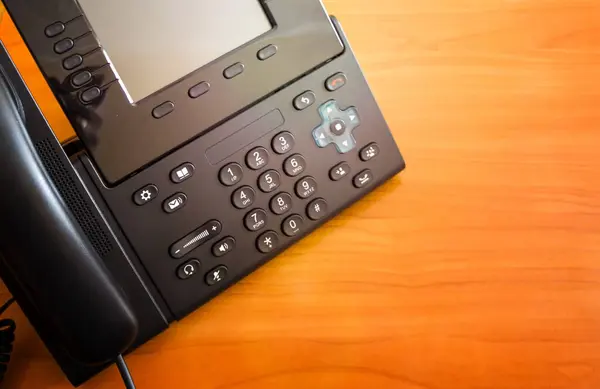 The black desktop push-button telephone. IP phone on desk in office. communication concept. close-up