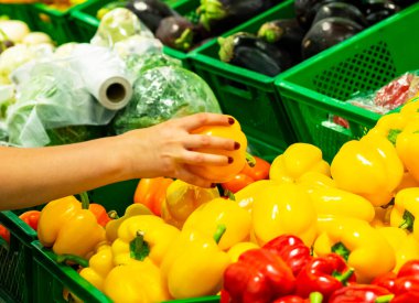 Kız elinde tatlı biber tutuyor. Kadın eli marketten sarı sebze alıyor. Yakın plan. Kadın bir mağazadan sebze seçiyor. Konsept alıcılar, alışveriş konsepti. biber almak