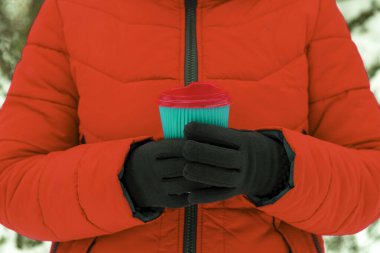 Kollar kahve ve kağıt bardak tutuyor. Karlı arka planda tek kullanımlık bir bardak tutan eller. Kış konseptine uygun kahve. Sıcak ve sıcak içecekler kış konseptinde.