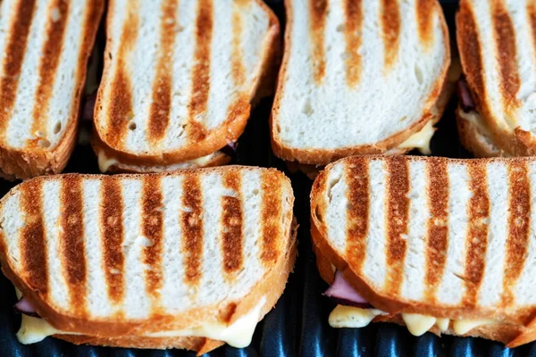Fried toasts with cheese. The silicone shovel takes toasts from a grill. toasted bread, sandwich on an electric grill. Fried toasts with orphaned and ham. closeup