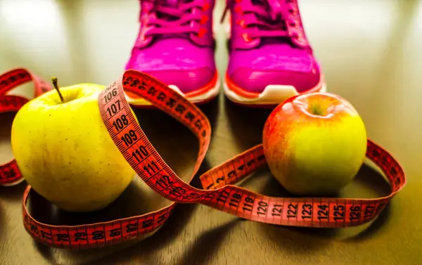 apples, meter tape, pink sneakers.  Fitness accessories. Measuring tape, centimeter.  The concept of joint sports, Healthy way of life.
