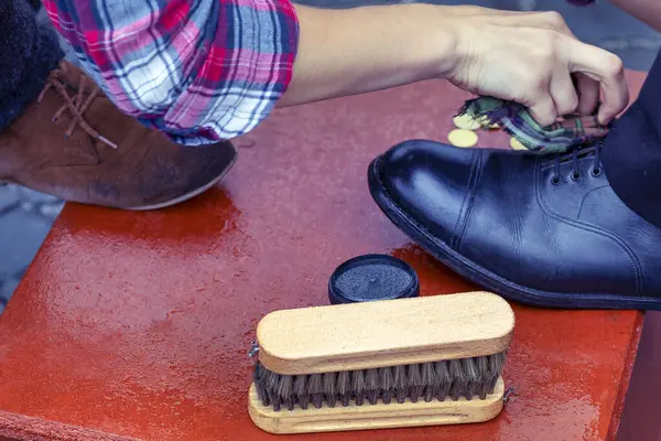 Shoe cream, brush close-up. Cleaning of boots on the street. Concept wrong care of footwear. Man\'s right foot shoe on traditional style boot scraper with brushes