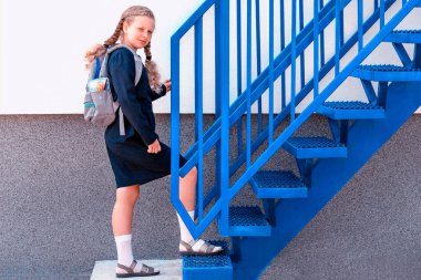 Liseli kız merdivenleri çıkıyor. Konsept okul günleri, başlangıç tarihi, sonraki aşama, kariyer merdiveni, başlangıç. Sırt çantalı üniformalı bir kız. Kız yukarı çık, bir adım yukarı.
