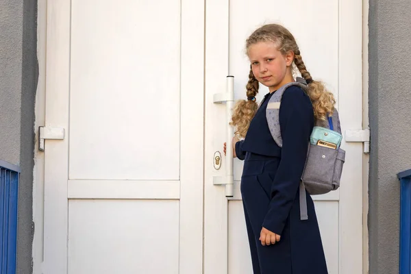 Schoolgirl near the school door, educational institution. Portrait of a  teenager on the background of the school. Concept Back to school. girl in a  uniform. pupil, learner, scholar. school entrance