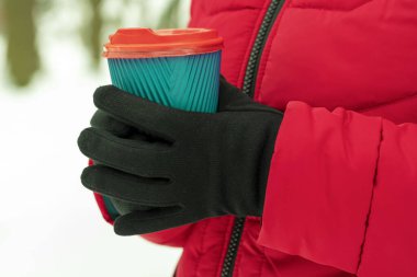 Kollar kahve ve kağıt bardak tutuyor. Karlı arka planda tek kullanımlık bir bardak tutan eller. Kış konseptine uygun kahve. Sıcak ve sıcak içecekler kış konseptinde.