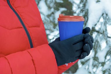 Kollar kahve ve kağıt bardak tutuyor. Karlı arka planda tek kullanımlık bir bardak tutan eller. Kış konseptine uygun kahve. Sıcak ve sıcak içecekler kış konseptinde.