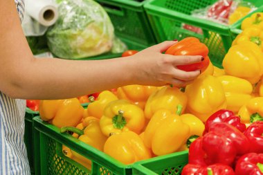 Kadın eli bir süpermarkette sebze alır. Yakın plan. Sarı tatlı biber tutan kız. Kadın bir mağazadan sebze seçiyor. Konsept alıcılar, alışveriş konsepti. biber almak