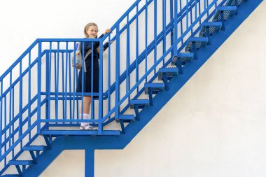 Gülümseyen kız öğrenci merdivenleri çıkıyor. Konsept okul günleri, başlangıç tarihi, sonraki aşama, kariyer merdiveni, başlangıç. Sırt çantalı üniformalı bir kız. Merdivenlerin yanındaki kız..