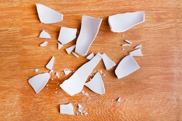 White Shards of a Broken Plate on the  background. splinters of a shattered Plate. Fragments of a white tableware on the floor. Shards and pieces of a broken dish. Top view