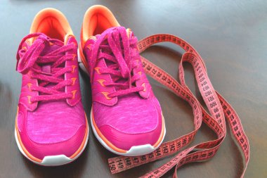 Kapatın. Metre şeridi, pembe spor ayakkabılar. Sağlıklı yaşam biçimi kavramı. Spor aksesuarları. Spor konsepti. Arka planda spor ayakkabılar. Rejimin ilk adımı ve sağlıklı bir yaşam tarzı..