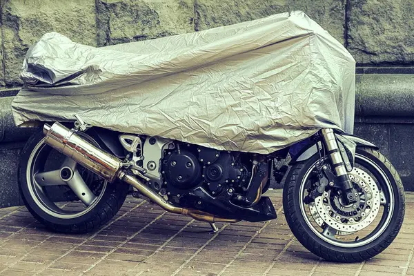 Covered Motorcycle. Parked motorcycle in a protective canvas, case. The motorbike covered with an oilcloth from a rain. Waterproof parking outdoors during travel.