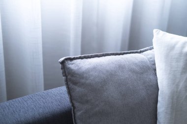 Rahat gri kanepede, yastıkların yakın çekimi. Oturma odasının modern iç mekanı. Büyük pencereli ve katıksız perdeli.