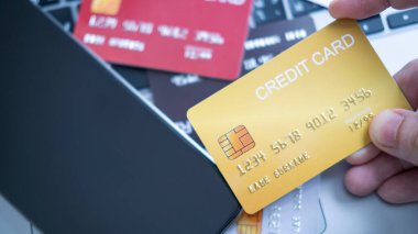 Bir el dizüstü bilgisayarın önünde kredi kartı tutuyor, online alışveriş ya da bankacılık olduğunu gösteriyor. Kartlar ve masanın üzerinde dijital ödemeler ve finansal işlemler kavramını vurgulayan bir akıllı telefon.