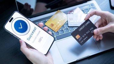 Bir akıllı telefon kullanarak çevrimiçi aktarımı tamamlar, bir Başarı iletisi görüntüler. Bilgisayardaki kredi kartları, başarılı dijital ödemeleri, online alışverişi, finansal işlemleri sembolize ediyor.