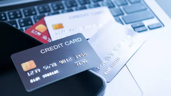 Farklı renklerde kredi kartı koleksiyonu, akıllı telefonun yanındaki dizüstü bilgisayarın klavyesinde. Finansal işlemlerde çoklu ödeme seçenekleri, dijital bankacılık ve güvenli çevrimiçi işlemler kavramı.