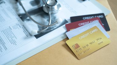 Tıbbi kayıtlara yakın kredi kartları ve steteskop, tıbbi masrafları maddi araçlarla ödeme kavramı.