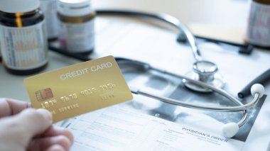 Tıbbi belgelere ve steteskopa sağlık ödemelerini sembolize eden siyah bir kredi kartı konmuş..