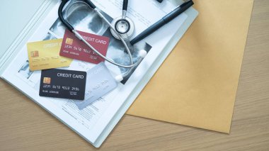 Hastane belgeleri ve steteskop üzerindeki kredi kartlarının çeşitliliği, sağlık hizmetleri ödemelerini vurguluyor.