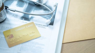 İlaç ve steteskop yanında tıbbi sipariş kağıdındaki altın kredi kartı, sağlık harcamalarını vurguluyor.