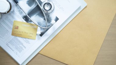 Steteskop, ilaç şişeleri ve evrak ile tıbbi raporlara yerleştirilmiş altın kredi kartı hastane ödemelerini ima ediyor..