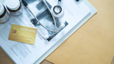 Steteskop ve ilaç şişeleriyle sağlık harcamaları ve finansal planlamayı temsil eden tıbbi belgelerde altın kredi kartı.