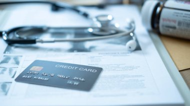 Arka planda steteskop ve ilaç şişeleri olan tıbbi belgelere gri bir kredi kartı yerleştirilmiş..