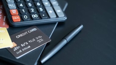 Closeup of black credit card near calculator and pen on desk reflecting focus on financial stability expense tracking and credit responsibility.