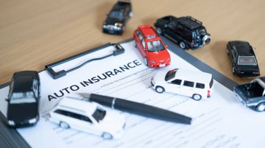 Auto insurance form with miniature cars and pen on wooden desk, symbolizing car insurance, safety, policy agreement and protection.