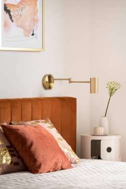 Şık yatak başlığı ve zarif yatak odasındaki komodinin üzerindeki dekorasyonla rahat bir yatağa yakın çekim yap.