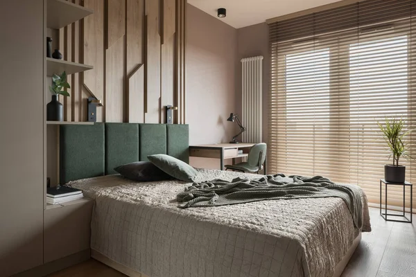 Aesthetic master bedroom with big window with wooden blinds, comfortable double bed, stylish decorations and desk to study
