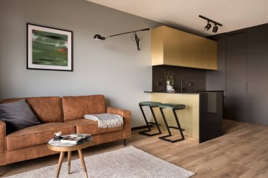 Kahverengi kanepeli rahat oturma odası siyah ve altın mobilyalı küçük mutfağa açık.