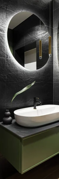 现代浴室的垂直全景 带有黑色墙砖 圆形镜子 带有铅光 椭圆形洗脸盆 装有绿色抽屉柜 — 图库照片
