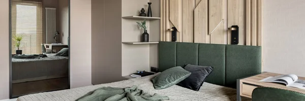 Panorama of cozy bedroom with mirror and decorative wooden wall behind bed with green headboard